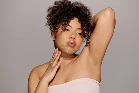 Eine atemberaubende Afroamerikanerin mit lockigem Haar posiert in einem Studio-Setting und strahlt Vertrauen und Schönheit aus.