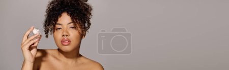 Young African American woman with curly hair holding jar of cream