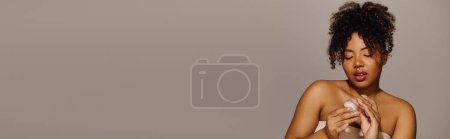 Téléchargez les photos : Une belle jeune afro-américaine aux cheveux bouclés drapés d'une serviette, exsudant élégance et grâce dans un cadre studio. - en image libre de droit