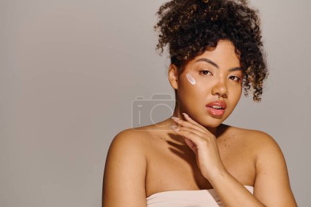 A beautiful young African American woman with curly hair draped in a white towel, delicately holds her hand to her face.