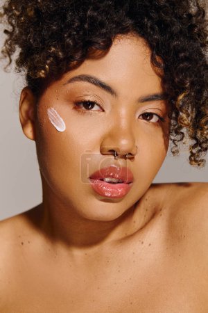A beautiful African American woman with curly hair showcasing a striking white cream on her cheek in a studio setting.