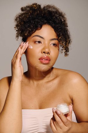 Téléchargez les photos : Une jeune afro-américaine aux cheveux bouclés tenant un bocal de crème devant son visage. - en image libre de droit