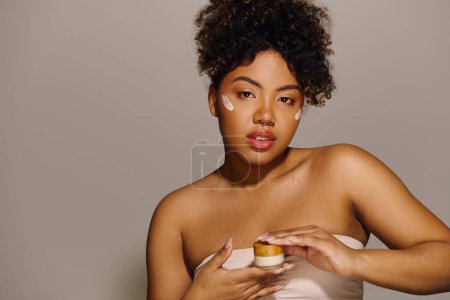 Photo for A beautiful young African American woman with curly hair delicately holds a jar of cream in her hands, focusing on skincare and beauty. - Royalty Free Image