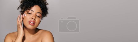 Photo for A beautiful young African American woman with curly hair, in a studio setting, holding her face in her hands. - Royalty Free Image