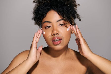 Téléchargez les photos : Une jeune femme afro-américaine aux cheveux bouclés tenant ses mains contre son visage dans une pose réfléchie. - en image libre de droit