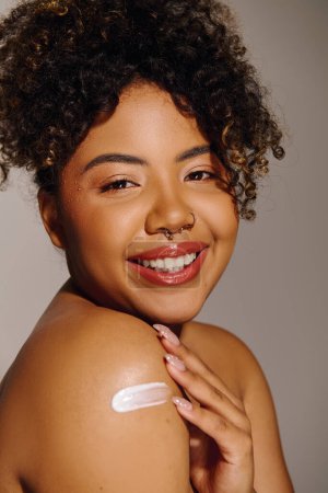 Téléchargez les photos : A young African American woman with curly hair showcasing a white cream on her arm in a striking studio setting. - en image libre de droit
