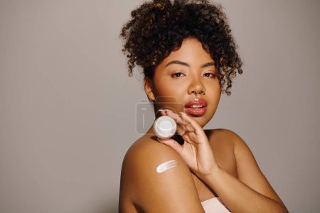 A beautiful young African American woman with curly hair in a studio setting, applying a thick layer of cream