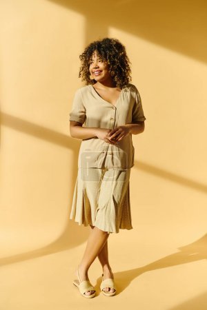 Eine schöne junge Afroamerikanerin mit lockigem Haar steht hoch in einem Raum mit einer leuchtend gelben Wand.
