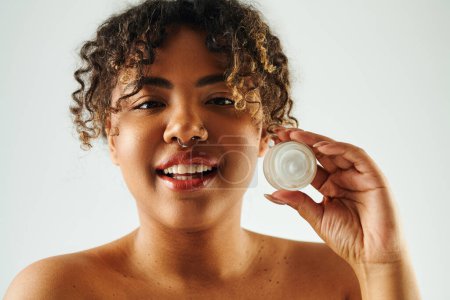 Una mujer afroamericana sosteniendo un frasco de crema frente a su cara.