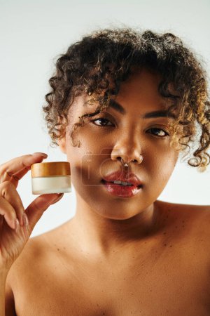 A beautiful African American woman holds a jar of cream in front of her face.