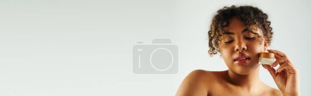 Photo for A beautiful African American woman poses holding a jar of cream. - Royalty Free Image