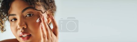 Foto de Mujer afroamericana con gracia toca su cara contra el vibrante telón de fondo. - Imagen libre de derechos