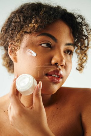 Woman gracefully applies cream to her face.