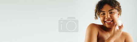 Photo for Alluring African American woman applying cream to her face - Royalty Free Image
