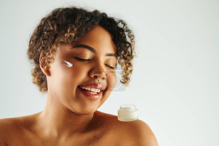 Foto de Cheerful African American woman smiling while holding a cream bottle. - Imagen libre de derechos
