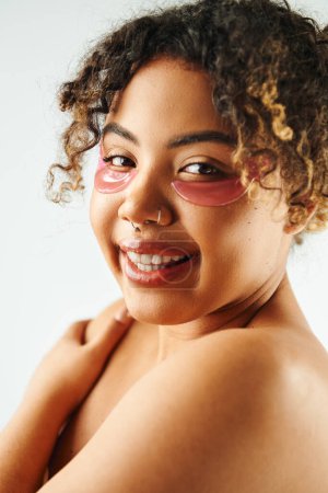 Cheerful African American woman showcasing eye patches on a vibrant backdrop.