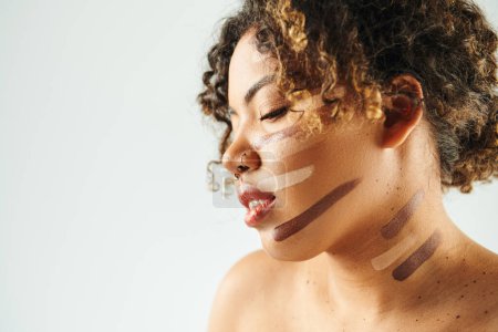 Appealing African American woman with foundation on face poses against vibrant backdrop.