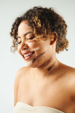 Attractive African American woman with foundation on face poses against vibrant backdrop.