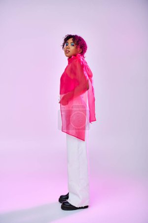 Téléchargez les photos : Femme afro-américaine en chemise rose et pantalon blanc posant sur un fond vibrant. - en image libre de droit
