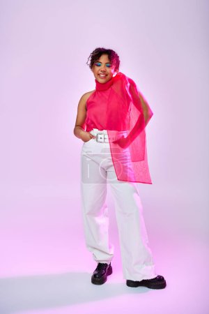 Femme afro-américaine pose gracieusement dans un pantalon blanc et haut rose sur fond vibrant.