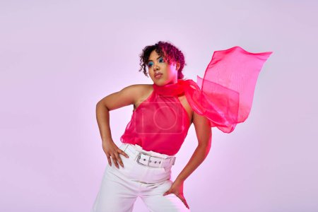 African American woman poses in white pants and pink top against vibrant backdrop.