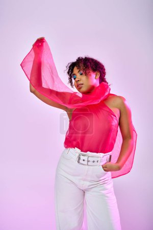 Una hermosa mujer afroamericana posa activamente en pantalones blancos y un top rosa sobre un vibrante telón de fondo.