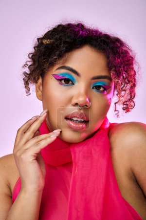 African American woman in pink top and blue eyeshadow poses vibrantly.