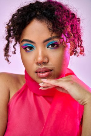 African American woman exudes beauty in pink top and blue eyeshadow against vibrant backdrop.