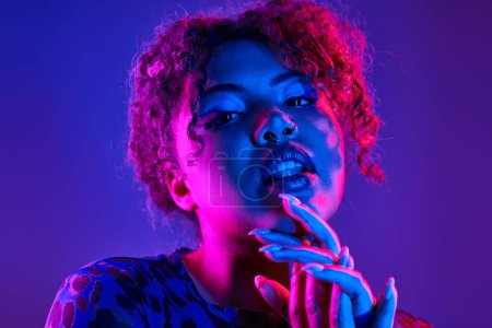 A striking African American woman poses with vibrant curly hair and bold blue makeup.