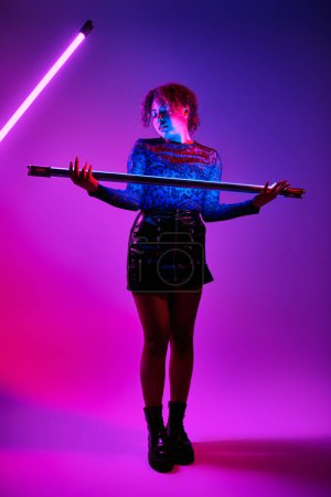 Une belle femme afro-américaine tient une lampe LED devant un fond violet vibrant.