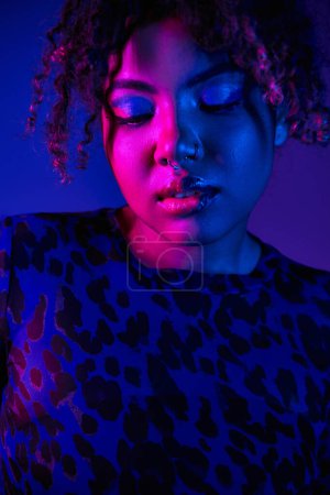 Téléchargez les photos : Une femme afro-américaine frappante aux yeux bleus portant une chemise imprimée léopard pose sur un fond vibrant. - en image libre de droit