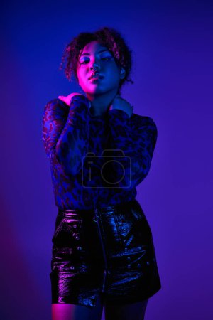 Photo for A beautiful African American woman poses actively against a vibrant purple backdrop. - Royalty Free Image