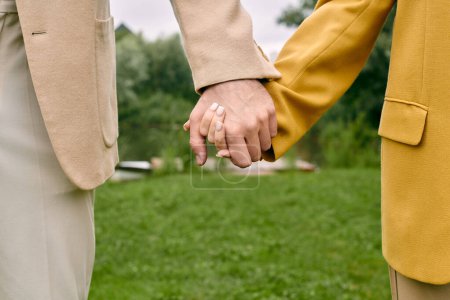 A close-up of two people, a beautiful couple, holding hands tenderly in a green park, showcasing love and connection.