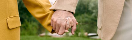 Eine Nahaufnahme von zwei Menschen, die sich an den Händen halten, ihre Finger ineinander verschränkt in einer wunderschönen grünen Parklandschaft.