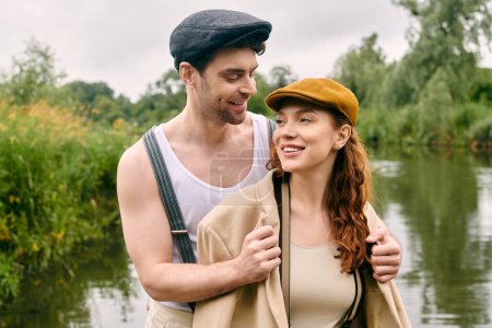 A man and woman standing by the river, enjoying a romantic date in a beautiful green park setting.