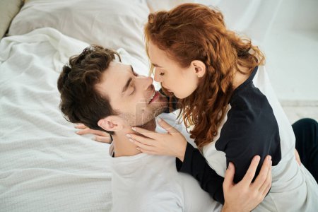 A man and a woman are peacefully embracing while laying on a bed in a bedroom setting.