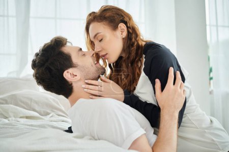 Foto de Un hombre besa tiernamente a una mujer en la mejilla, expresando amor e intimidad en un ambiente acogedor dormitorio. - Imagen libre de derechos