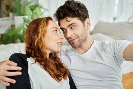 Un homme et une femme assis sur un lit, se regardant avec un sentiment d'amour et de connexion.