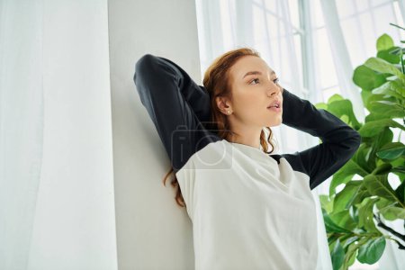 Une femme se penche contre un mur avec sa main sur la tête, perdue dans la pensée.