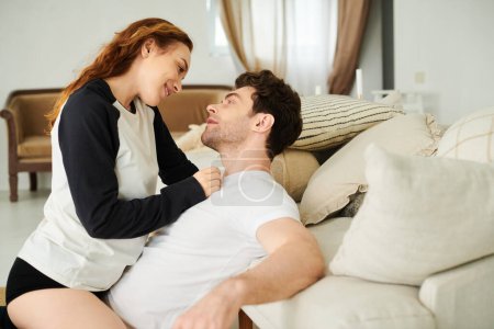 Foto de Una pareja se relaja pacíficamente, con un hombre sentado encima de un sofá junto a una mujer en un entorno de dormitorio. - Imagen libre de derechos