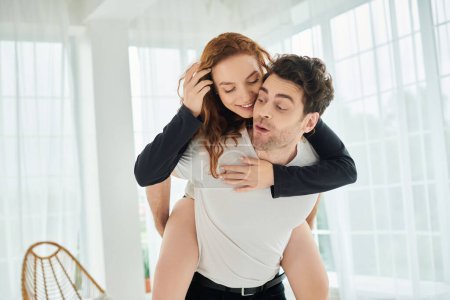 Foto de Un hombre sostiene a una mujer en sus brazos, rodeada de un ambiente cálido e íntimo en un dormitorio. - Imagen libre de derechos