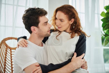 Un hombre y una mujer abrazándose tiernamente, expresando amor y cercanía en un entorno de dormitorio sereno.