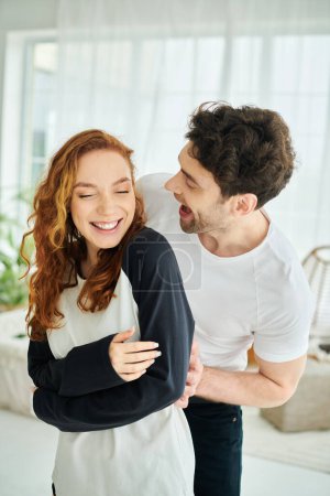 Ein Mann und eine Frau teilen sich einen Moment der Freude und lachen gemeinsam in ihrem gemütlichen Wohnzimmer.