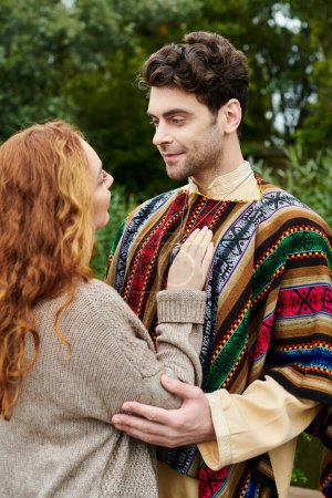 A man and a woman in boho attire stand together in a green park, surrounded by serene beauty.