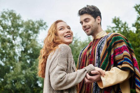 A romantic date between a man and a woman dressed in boho style clothing, surrounded by lush greenery in a natural setting.