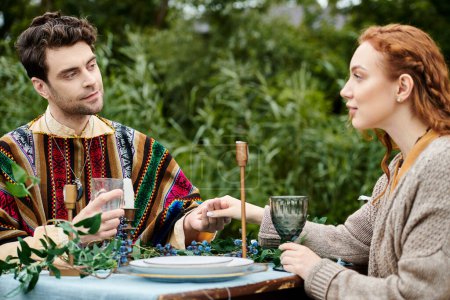 Ein Mann und eine Frau in Boho-Kleidung sitzen an einem Tisch in einem üppig grünen Park und genießen ein romantisches Date.