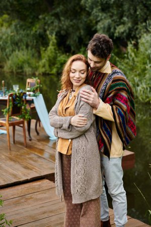 A man and a woman, dressed in boho style clothes, sharing a peaceful hug on a quiet dock by a serene lake.