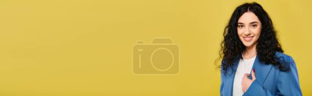 Téléchargez les photos : Une femme brune aux cheveux bouclés dans un costume bleu frappant une pose, exprimant des émotions dans un cadre de studio avec un fond jaune. - en image libre de droit