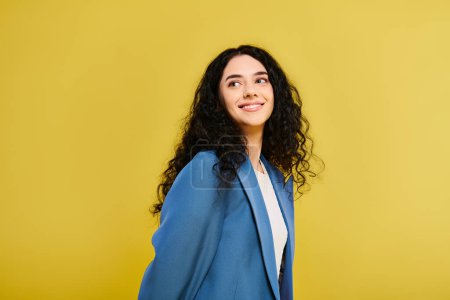Une jeune femme brune vêtue d'une veste bleue se tient en confiance devant un mur jaune frappant, respirant style et émotion.