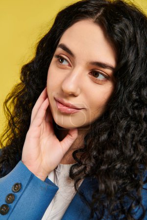 Foto de A young woman with curly hair poses in a studio, showcasing emotions while wearing a blue jacket against a yellow background. - Imagen libre de derechos